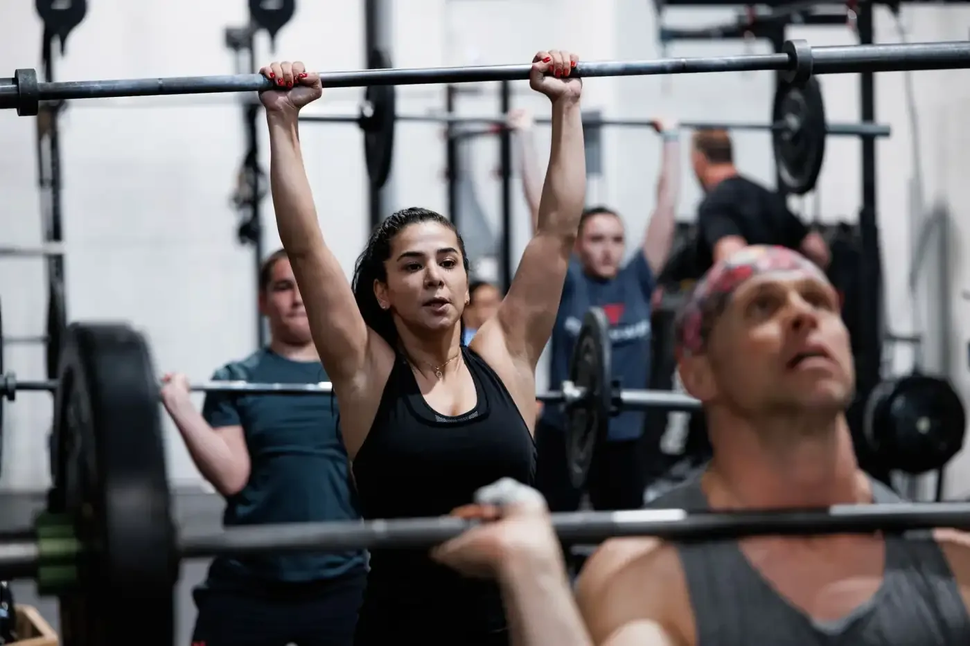 A full class pressing barbells overhead together at FirePower