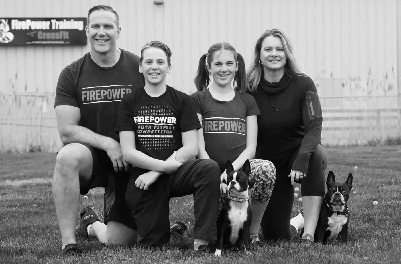 The FirePower founding family kneeling on the grass with their two dogs outside the gym
